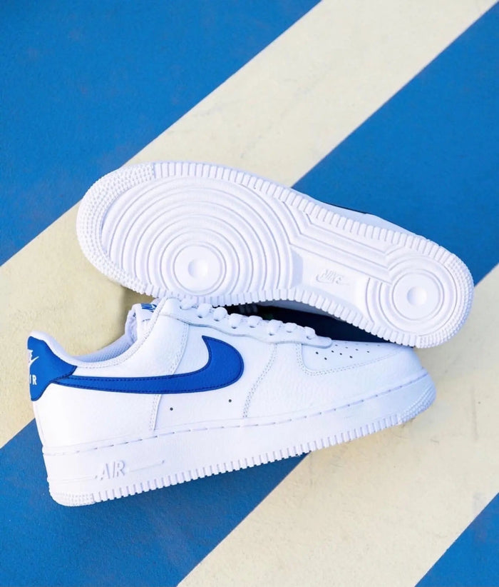 White low-top sneakers with blue Nike swoosh, white rubber sole, and lace-up