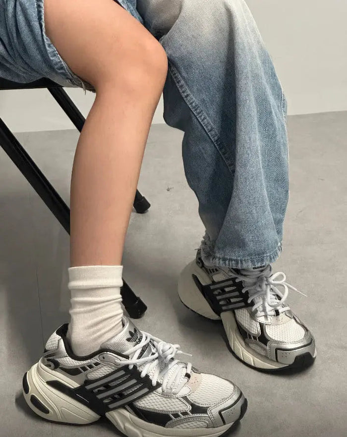 White and dark gray running shoes on feet with white socks and blue jeans