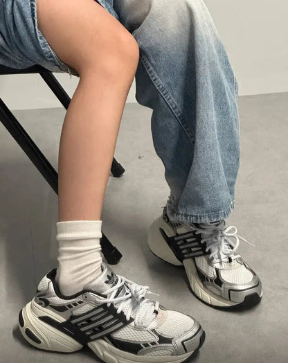 White and dark gray running shoes on feet with white socks and blue jeans
