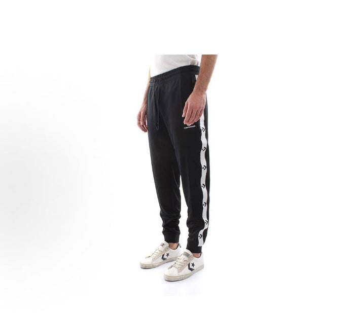 Black track pants with white side stripe and tapered fit, paired with sneakers
