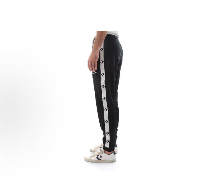 Black track pants with vertical white side stripe, worn with light sneakers