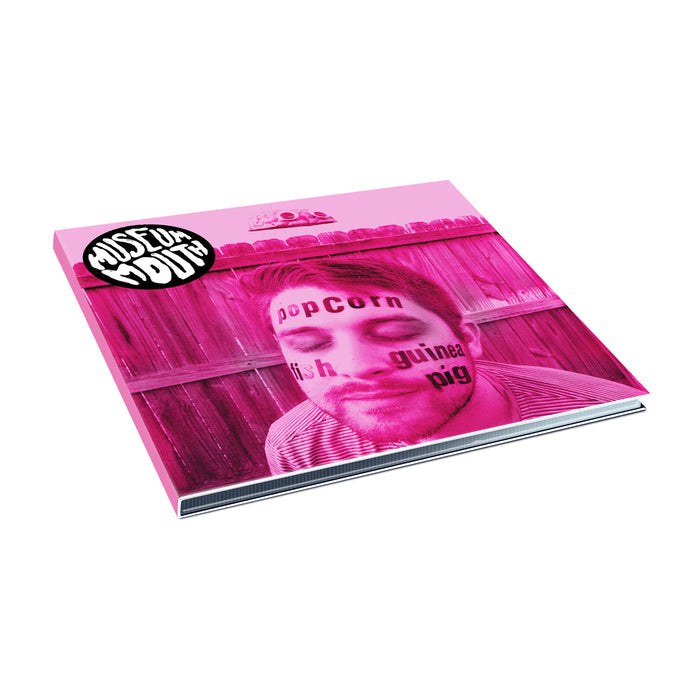 A pink-tinted album cover by Museum Mouth shows a close-up of a man's face with "Popcorn Fish Guinea Pig" written on his skin, a wooden fence in the background, plus the MUST FUN YOUTH logo and CD Track List in the corner.